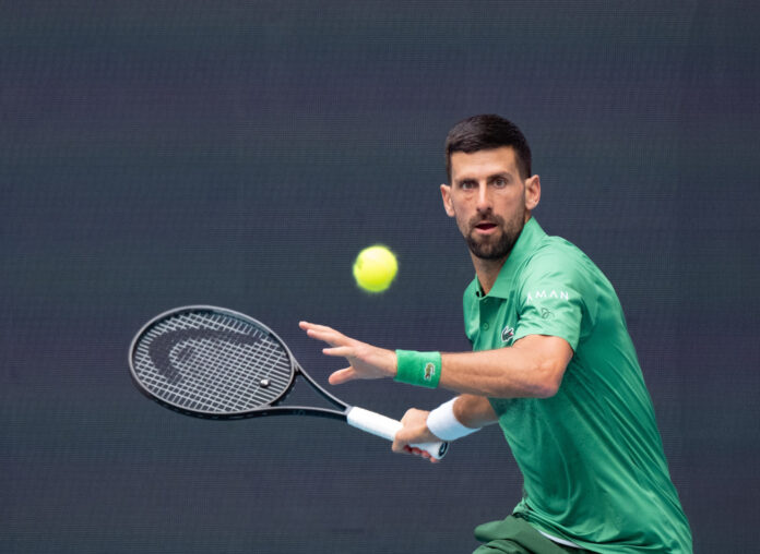 Novak Djokovic prepares to hit a forehand volley during a match at the Miami Open, wearing a green polo shirt and matching wristbands.