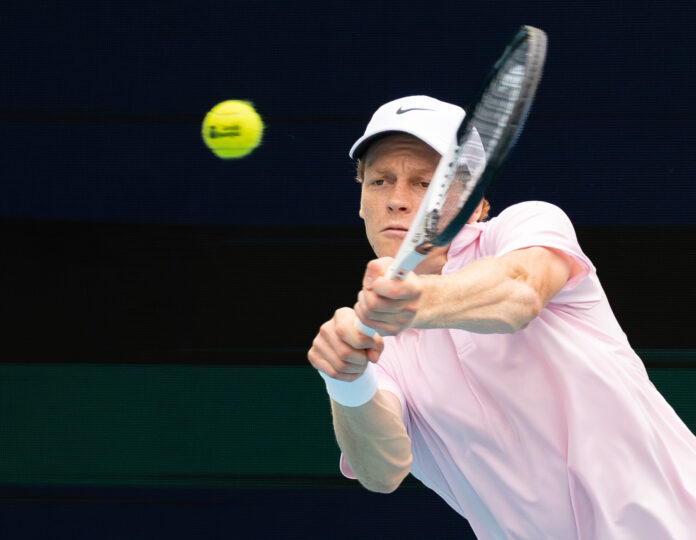 Jannik Sinner hits a two-handed backhand in a pink shirt and white cap at the 2026 Miami Open, eyes fixed on the ball — the world No. 1 who has now spent 81 weeks at the top of the ATP rankings.