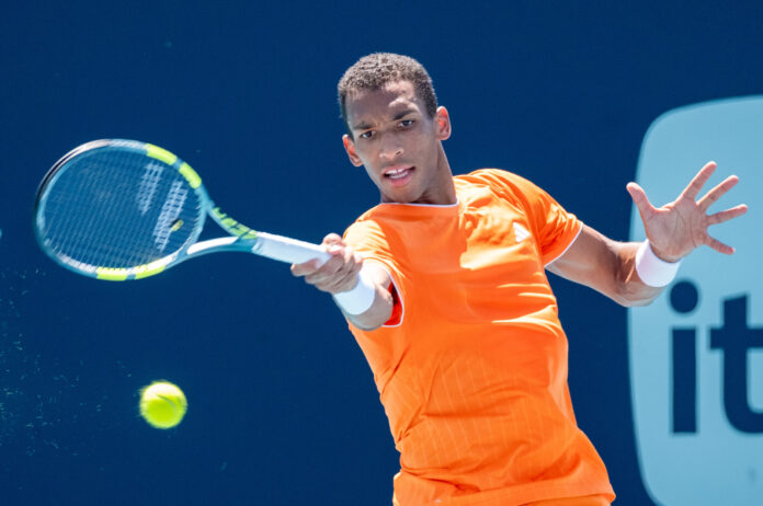 Felix Auger-Aliassime stretches for a forehand in an orange kit on a blue hard court at the Miami Open.