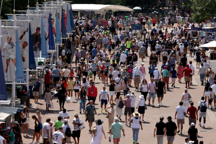 Crowds of spectators walking a wide plaza lined with US Open champions banners at the USTA Billie Jean King National Tennis Center in 2022