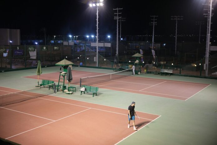 Several hard tennis courts lit by floodlights at night